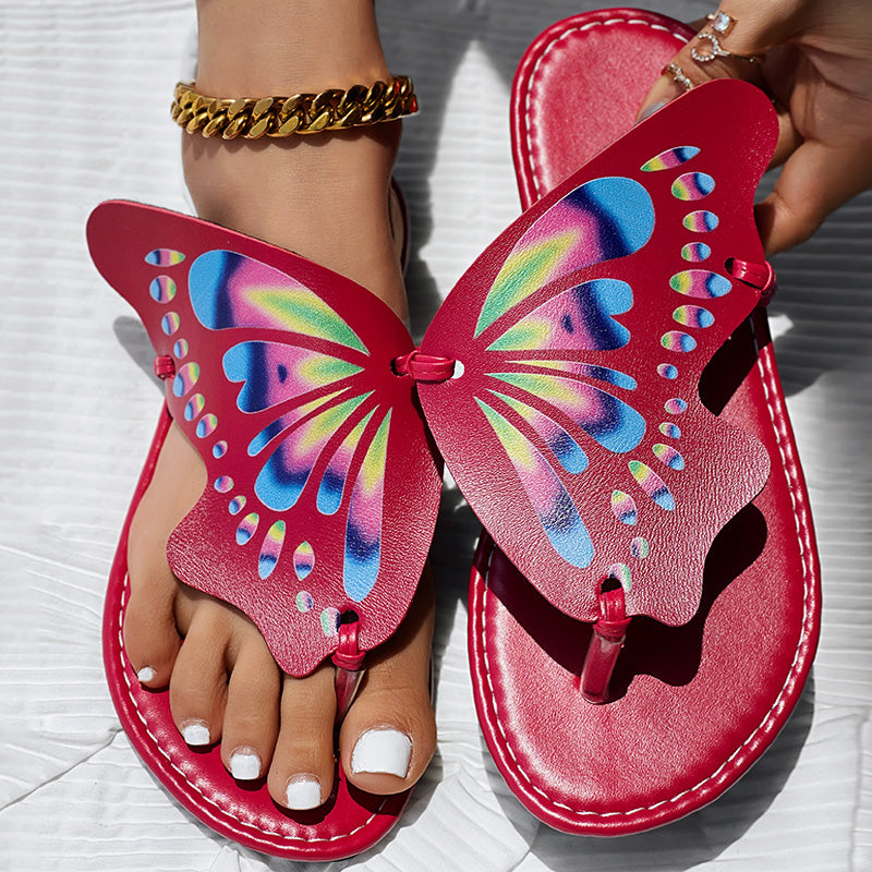 Red butterfly wing flip flops with colorful tie-dye pattern, worn on feet with white nails and gold anklet