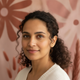 Close-up portrait of a smiling woman, late 20s to early 30s, with a soft, blurred background in terracotta, rose, and blush p