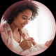 Close-up portrait of a content young mother gently holding her baby's hand, looking down with a caring expression.